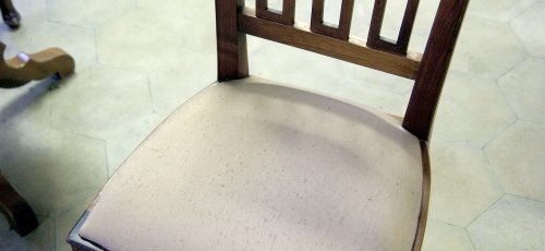 Cadira de fusta amb plafons tallats a mà, seient entapissat i respatller inclinat. Fabricat en fusta de noguer