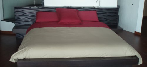 Cama habitación. Cabezal con ranuras rebajadas a mano y mesitas integradas con cajones. Colchón enmarcado en madera. Fabricado en madera de roble macizo teñido.